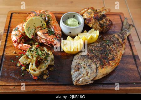 Piatto di frutti di mare misti con gamberi tigre, calamari e pesce alla griglia intero guarnito con limone e salsa Foto Stock