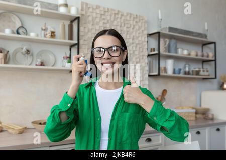 Ragazza che mostra un inalatore per asmatici seduta su un divano nel salotto di casa Foto Stock