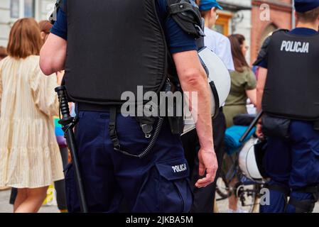 Poliziotto in uniforme con pistola e manette mantiene ordine a dimostrazione in strada in Polonia. L'ufficiale di polizia guardia folla di persone alla sfilata Foto Stock