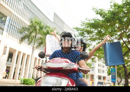 Felice coppia latino-americana con borse di carta a cavallo in scooter in città Foto Stock