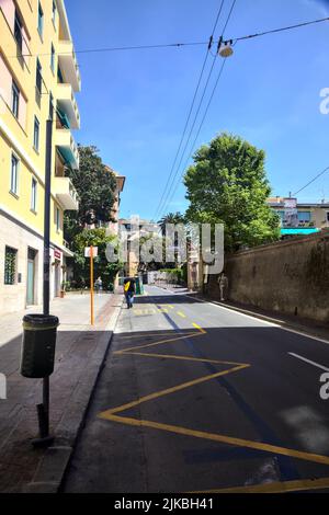 Strada con edifici alti e un muro di pietra in una giornata limpida Foto Stock