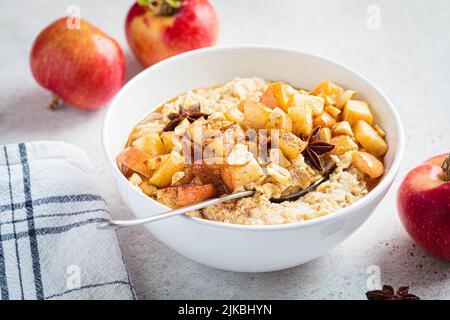 Fiocchi d'avena autunnali con mela caramellata e cannella in ciotola bianca. Ricetta invernale accogliente. Cibo sano e confortevole. Foto Stock