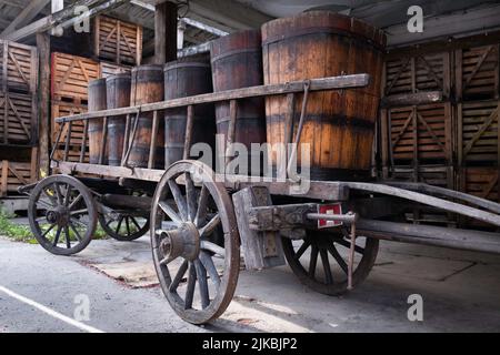 Vecchie botti di vino di legno su un carrello di legno nella città francese di Ribeauvillé in Alsazia. Casse in un fienile in background Foto Stock