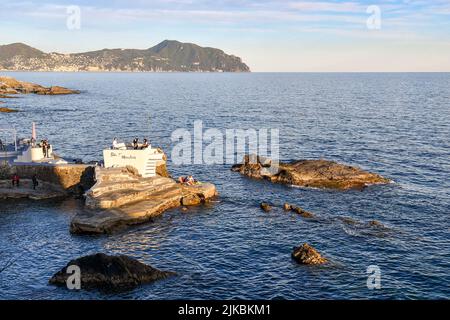 Vista sul Golfo Paradiso con persone in un bar all'aperto su una scogliera della passeggiata Anita Garibaldi e del promontorio di Portofino, Nervi, Genova Foto Stock