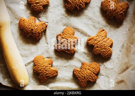 Ci sono diversi biscotti fatti in casa di farina d'avena fresca sotto forma di uomini di pan di zenzero su una teglia da forno con carta da forno, e un perno di legno si trova nex Foto Stock