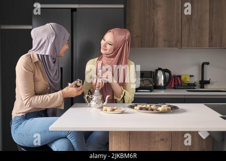 Due donne musulmane parlano, bevono il tè e mangiano dolci arabici. Foto Stock