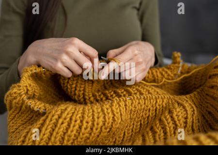 Primo piano del maglione di lana per maglieria femminile a mani. Donna si maglia da filo spesso. Abiti fatti a mano. La ragazza entra per i suoi hobby. Unione Foto Stock