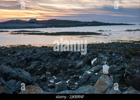 Un uomo che guarda il sole tramontare sull'isola di Lihou da l'Erée, Guernsey, Isole del canale Foto Stock