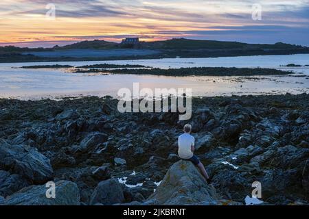 Un uomo che guarda il sole tramontare sull'isola di Lihou da l'Erée, Guernsey, Isole del canale Foto Stock