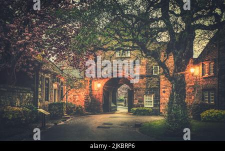 Gli edifici storici di Abbey Gatehouse e del Registro dei Vescovi visti nel terreno del distretto della Cattedrale di Carlisle in primavera con la fioritura circostante Foto Stock