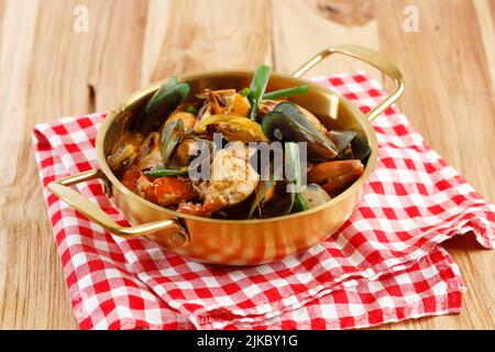 Red Seafood Jjampong, zuppa di noodle di pesce speziato cinese coreano con verdure, servita su Gold Pan. Messa a fuoco selettiva Foto Stock