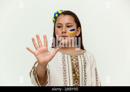 Una ragazza in un abito ricamato si erge sullo sfondo di un muro bianco, mettendo la mano destra in avanti Foto Stock