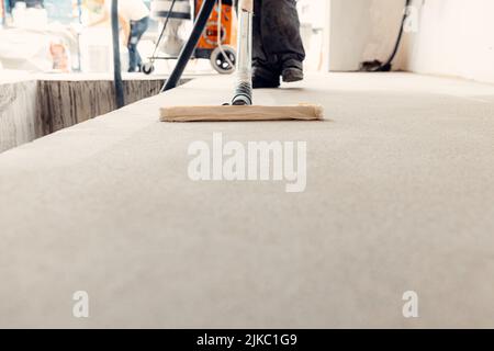 Un primo piano di un lavoratore che prepara il pavimento per la pittura Foto Stock