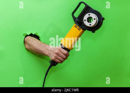 Attrezzo per il taglio della filettatura. Una mano su sfondo verde contiene un utensile elettrico per il taglio di filettature su metallo. Foto Stock