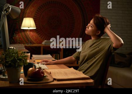 Studentessa collegiale femminile che utilizza il computer mentre fa i compiti a casa a tarda notte Foto Stock