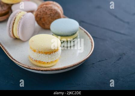 Macaron francesi colorati su piatto su sfondo nero Foto Stock