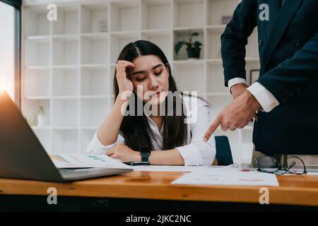 Furious boss spolding giovani frustrati interni. Operai inefficaci dell'ufficio seduti al tavolo e ascoltando il capo irritato urlando con annoiato e. Foto Stock