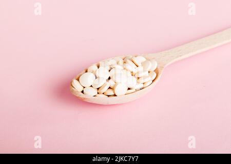 Mucchio di pillole bianche su sfondo colorato. Compresse sparse su un tavolo. Pila di capsule rosse di gelatina molle. Vitamine e supplementi dietetici concetto. Foto Stock