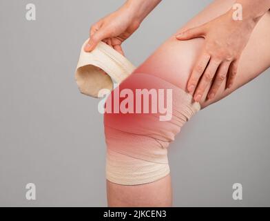 Donna che avvolge un bendaggio elastico intorno al ginocchio doloroso per alleviare il dolore o prevenire lesioni. Donna che soffre di fastidio alle gambe. Legamenti a spruzzo, cartilagine lacerata. Foto di alta qualità Foto Stock