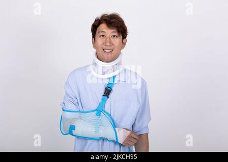 Ritratto di un bell'uomo asiatico sorridente con braccio rotto e collo isolato su sfondo bianco copia spazio Foto Stock