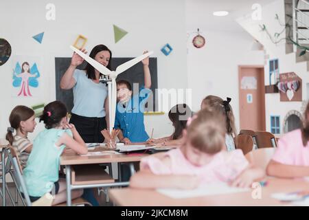 Scuola elementare STEM Robotics Classroom Gruppo diversificato di bambini costruzione e programmazione di mulino a vento ecologia robot concetto. Insieme parlando e. Foto Stock