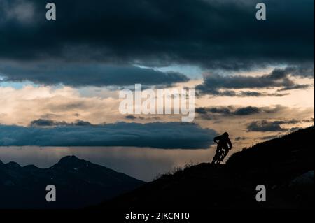 Mountain Biker in curva su Ridgeline in Loomy Alpine Vista Foto Stock