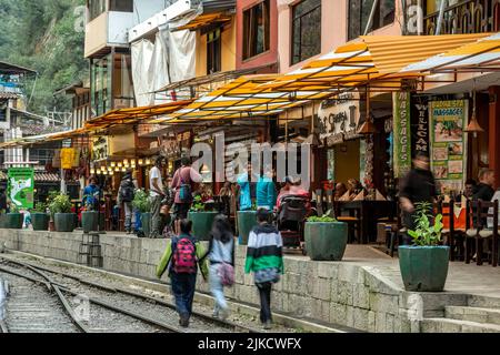 Fila di ristoranti, gente e treni, Aguas Calientes, aka Machu Picchu Pueblo, Urubamba, Cusco, Perù Foto Stock