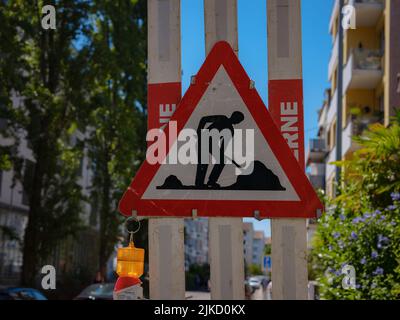 Uomo al lavoro Sign on Road. Cartello segnaletico costruzione su strada stradale sfocata con sfondo colorato bokeh leggero astratto. Copiare lo spazio di trasporto a Foto Stock