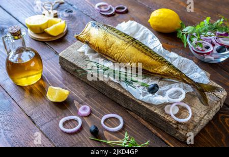 Sgombro affumicato su supporto in legno, anelli di cipolla, limone, olive, olio d'oliva, rosmarino su sfondo di legno Foto Stock