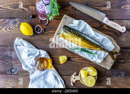 Sgombro affumicato su supporto in legno, anelli di cipolla, limone, olive, olio d'oliva, rosmarino su sfondo di legno Foto Stock
