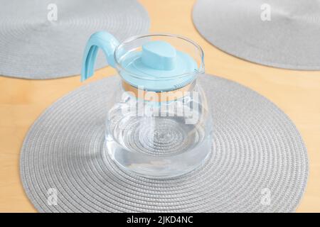 Una moderna caraffa trasparente blu chiaro piena di acqua potabile fresca e pulita che si stesa sul tavolo, primo piano, nessuno, nessuna gente. wat. Bevente Foto Stock