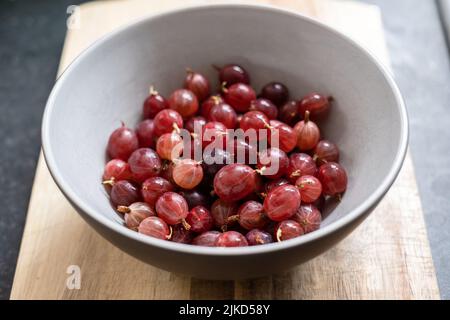 Una ciotola di frutti di bosco rossi Hinnonmaki appena raccolti e lavati su un tagliere di legno. Foto Stock