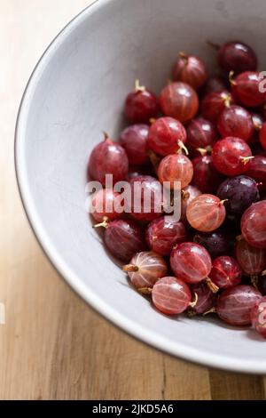 Una ciotola di frutti di bosco rossi Hinnonmaki appena raccolti e lavati su un tagliere di legno. Foto Stock