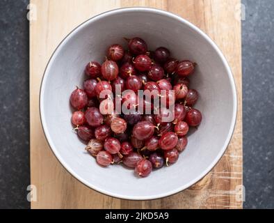 Una ciotola di frutti di bosco rossi Hinnonmaki appena raccolti e lavati su un tagliere di legno. Foto Stock