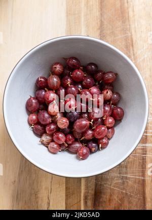 Una ciotola di frutti di bosco rossi Hinnonmaki appena raccolti e lavati su un tagliere di legno. Foto Stock