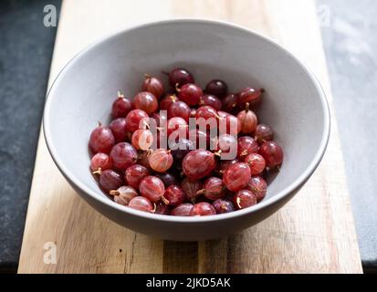 Una ciotola di frutti di bosco rossi Hinnonmaki appena raccolti e lavati su un tagliere di legno. Foto Stock