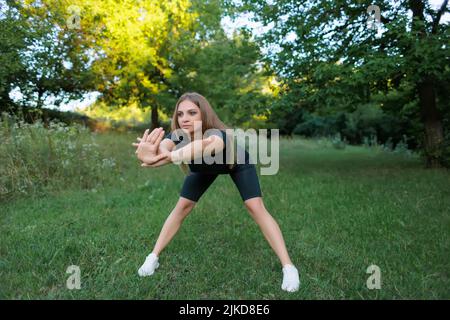 bella ragazza sportiva nel parco è impegnata in forma facendo curve in avanti Foto Stock