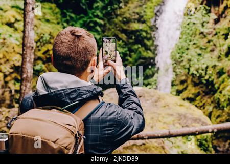 Uomo che prende la foto di cascata scenografica con il suo telefono Foto Stock
