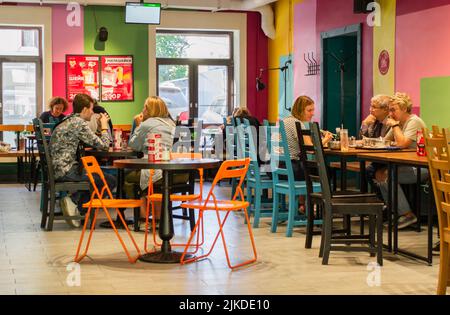 Mosca, Russia, 2019 agosto: La gente si siede all'interno dei caffè ai tavoli e parla. L'interno del cafe' con pareti luminose e arredamento colorato. Foto Stock
