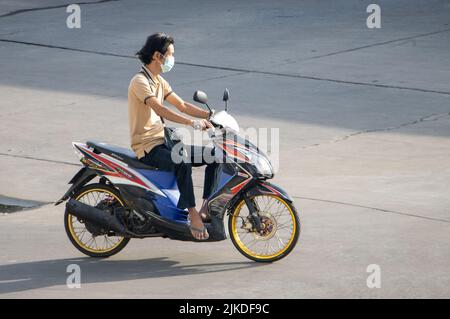 SAMUT PRAKAN, THAILANDIA, 30 2022 MAGGIO, Un uomo con maschera di faccia corre una moto nella strada soleggiata Foto Stock