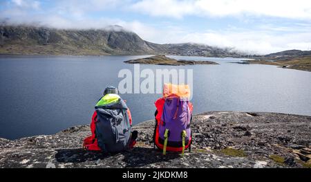 Vista panoramica del lago e della città di Qaqortoq, Groenlandia con coppia di backpackers in primo piano, il 13 luglio 2022 Foto Stock