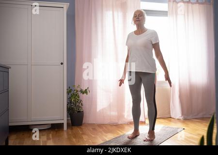 Donna anziana che lavora fuori in piedi in interni a Tadasana, posa di montagna. Foto Stock