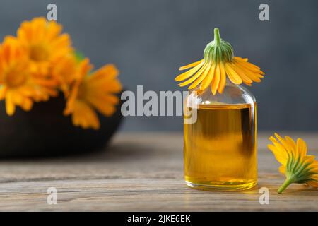 Bottiglia di olio essenziale di calendula o infusione e fiori marigold su sfondo. Medicina alternativa di erbe. Foto Stock