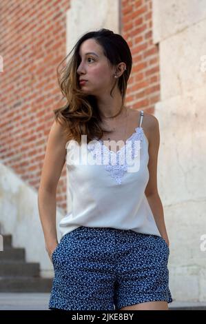 Giovane donna che cammina attraverso i giardini di Sabatini a Madrid. Donna che cammina con pantaloncini blu e blusa bianca Foto Stock