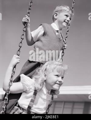 1950S BIONDA RAGAZZO E RAGAZZA SUL CAMPO DA GIOCO SWING SET RAGAZZA SEDUTA SUL SEDILE SWING E RAGAZZO IN PIEDI DIETRO DI LEI - J7551 HAR001 HARS 1 SEDILE GIOVANE ELEMENTARE BIONDA AMICO EQUILIBRIO LAVORO DI SQUADRA FELICE GIOIA LIFESTYLE FEMMINE FRATELLI SALUTE COPIA SPAZIO AMICIZIA PERSONE DI MEZZA LUNGHEZZA MASCHI FRATELLI SORELLE B&W SCUOLE GRADO FELICITÀ ALLEGRO ED ECCITAZIONE RECESSO RICREAZIONE FRATELLO GEMELLAGGIO SORRISI CONNESSIONE AMICHEVOLE GIOIOSO SCUOLA DI GRADO UNIONE NERO E BIANCO ETNIA CAUCASICA HAR001 VECCHIO STILE Foto Stock