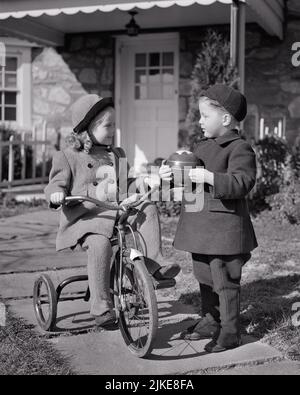 1940S RAGAZZA CHE RIDE TRICICLO SUL MARCIAPIEDE CHE PARLA CON IL RAGAZZO CHE TIENE UNA PALLA ENTRAMBI INDOSSANDO CAPPOTTI INVERNALI CAPPELLI DI FRONTE DI CASA - J8836 HAR001 HARS COMUNICAZIONE AMICO GIOIA LIFESTYLE FEMMINE CASE FRATELLI CAPPOTTI SALUBRITÀ HOME VITA COPIA SPAZIO AMICIZIA FULL-LENGTH ISPIRAZIONE RESIDENZIALE MASCHI EDIFICI FRATELLI TRASPORTO SORELLE B&W VICINI FELICITÀ TRICICLO ESTERNO SCHIACCATE CASE FRATELLO SORELLA AMICHEVOLE RESIDENCE ELEGANTE IN FRONTE DI PIETRA CASA CRESCITA GIOVANI TOGETHERNESS TRIKE NERO E BIANCO ETNIA CAUCASICA HAR001 VECCHIO STILE Foto Stock