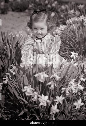 1940S 1950S BAMBINA IN ABITO A RIGHE IN CAMPO FIORITO PIENO DI NARCISI PRIMAVERILI CHE SQUINTING GUARDANDO LA MACCHINA FOTOGRAFICA - J814 HAR001 HARS NATURA COPIA SPAZIO A METÀ LUNGHEZZA STRISCE B&W OCCHIO CONTATTO FELICITÀ ALLEGRO ANGOLO ALTO SQUINTING DAFFODILS SORRISI GIOIOSO ELEGANTE PIACEVOLE PIACEVOLE AFFASCINANTE CRESCITA GIOVANI LOVABLE PIACEVOLE PRIMAVERA GIOVANE ADORABILE ATTRAENTE BIANCO E NERO ETNIA CAUCASICA HAR001 VECCHIO STILE Foto Stock