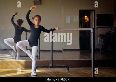 1980S GIOVANE STUDENTESSA DI BALLETTO AFRO-AMERICANA CHE PRATICA ALLA BARRA GUARDANDO LA MACCHINA FOTOGRAFICA RIFLESSA NELLO SPECCHIO - KD5122 NET002 HARS VECCHIO STILE PRATICANTE AFROAMERICANI Foto Stock