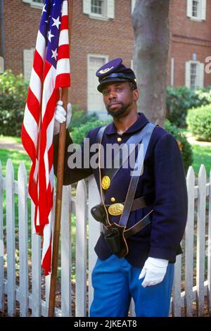 1990S AFRICAN AMERICAN MAN UNION SOLDATO UNIFORME GUERRA CIVILE REENACTOR GUARDANDO LA FOTOCAMERA TENENDO BANDIERA AMERICANA PHILADELPHIA PA USA - KP6430 NET002 HARS MEZZA LUNGHEZZA PERSONE MASCHI OCCHIO CONTATTO LIBERTÀ GUERRE AVVENTURA UNIONE AFRICANO-AMERICANI AFRO-AMERICANI ESTERNO PA NERO ETNIA VISO CAPELLI UNIFORMI RICORDO CONCETTUALE 1860S NERI STELLE E STRISCE REENACTOR CONTRIBUTO UNIFORME VECCHIA GLORIA BARBA ROSSO BIANCO E BLU GIOVANE ADULTO GUERRA CIVILE AMERICANA LA BANDIERA AMERICANA BATTE I CONFLITTI DI GUERRA CIVILE GLI AFROAMERICANI IN VECCHIO STILE Foto Stock