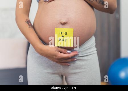 primo piano di vista di una donna incinta del ventre con una nota appiccicosa che dice che è un ragazzo. Foto di alta qualità Foto Stock
